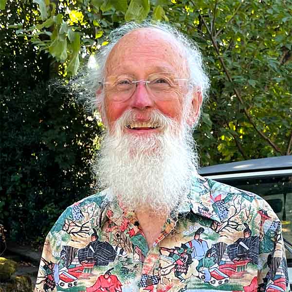 David stands in front of his beloved 1989 Jeep Wrangler in a colorful, printed shirt. His long, white hair and beard are slightly windswept and he has a friendly smile on his face.