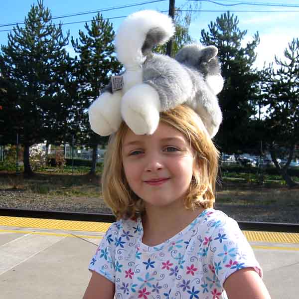 Throwback photo of Erin at 6 years old, standing on a train station platform with a stuffed animal wolf on her head, butt inexplicably towards the camera. She has a smile on her face that suggest she’s proud of herself.